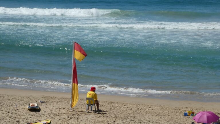 lifeguard-sitting-on-beach-next-to-flag-looking-ou-2021-10-13-23-45-41-utc